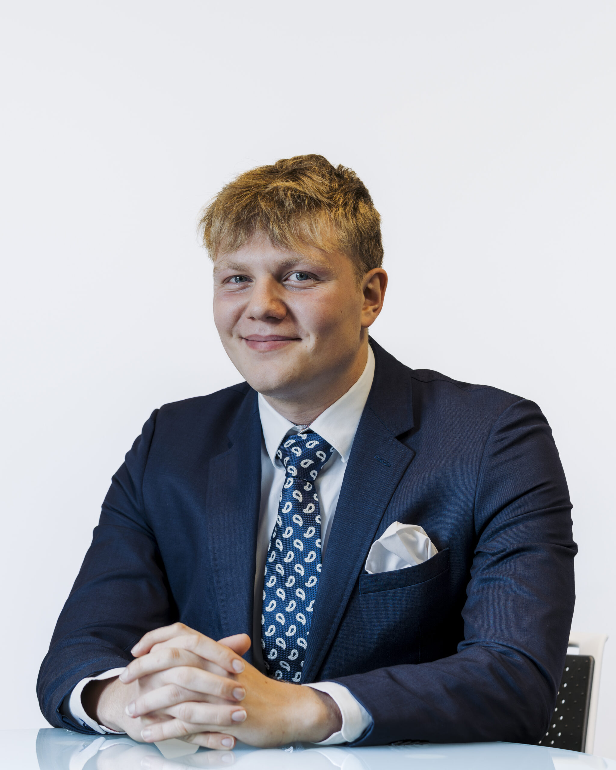 Archie, finance specialist at LendFirst, seated at a desk in a navy suit and patterned tie, focused on helping clients secure fast, flexible bridging loans.